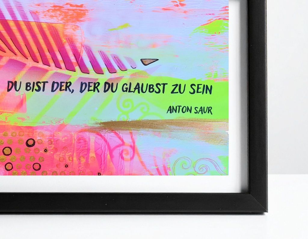 Bunter Kunstdruck mit dem Zitat "Du bist der, der du glaubst zu sein" von Anton Saur, eingerahmt mit schwarzem Rahmen auf weißem Untergrund.